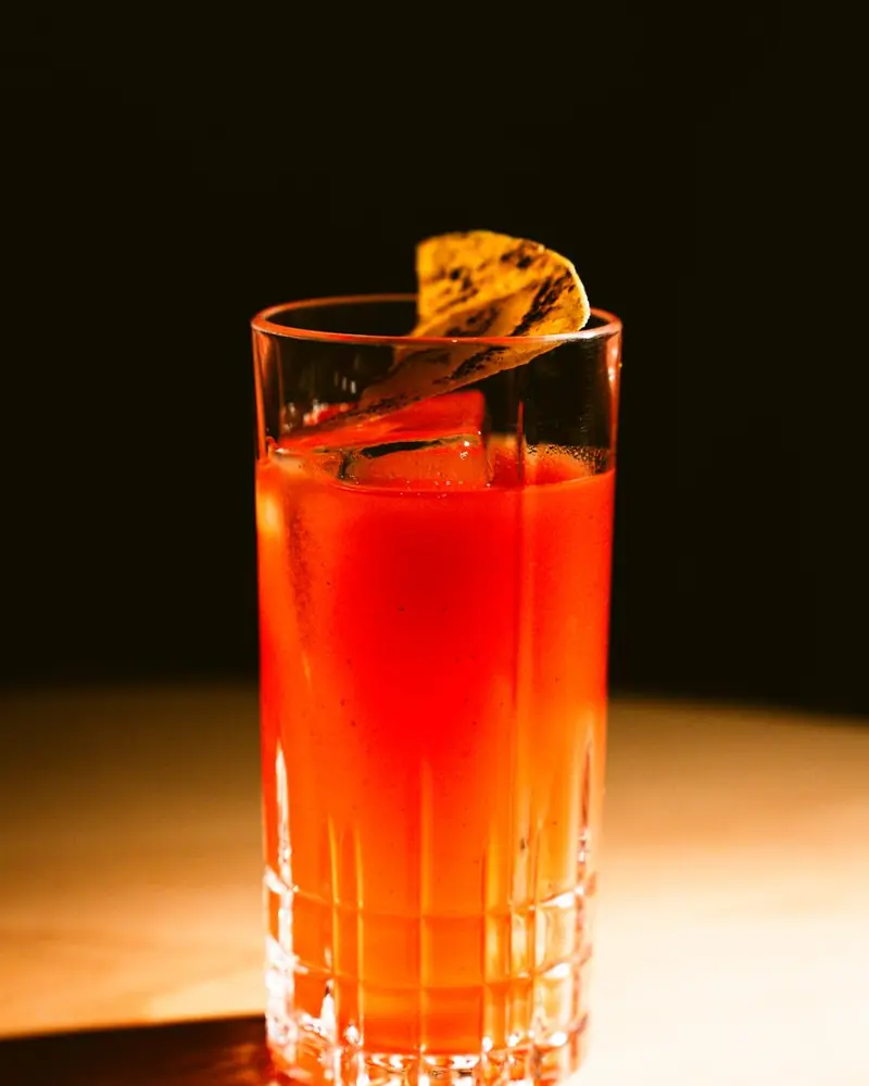 Hohes geschliffenes Glas mit rotem Longdrink und Zeste