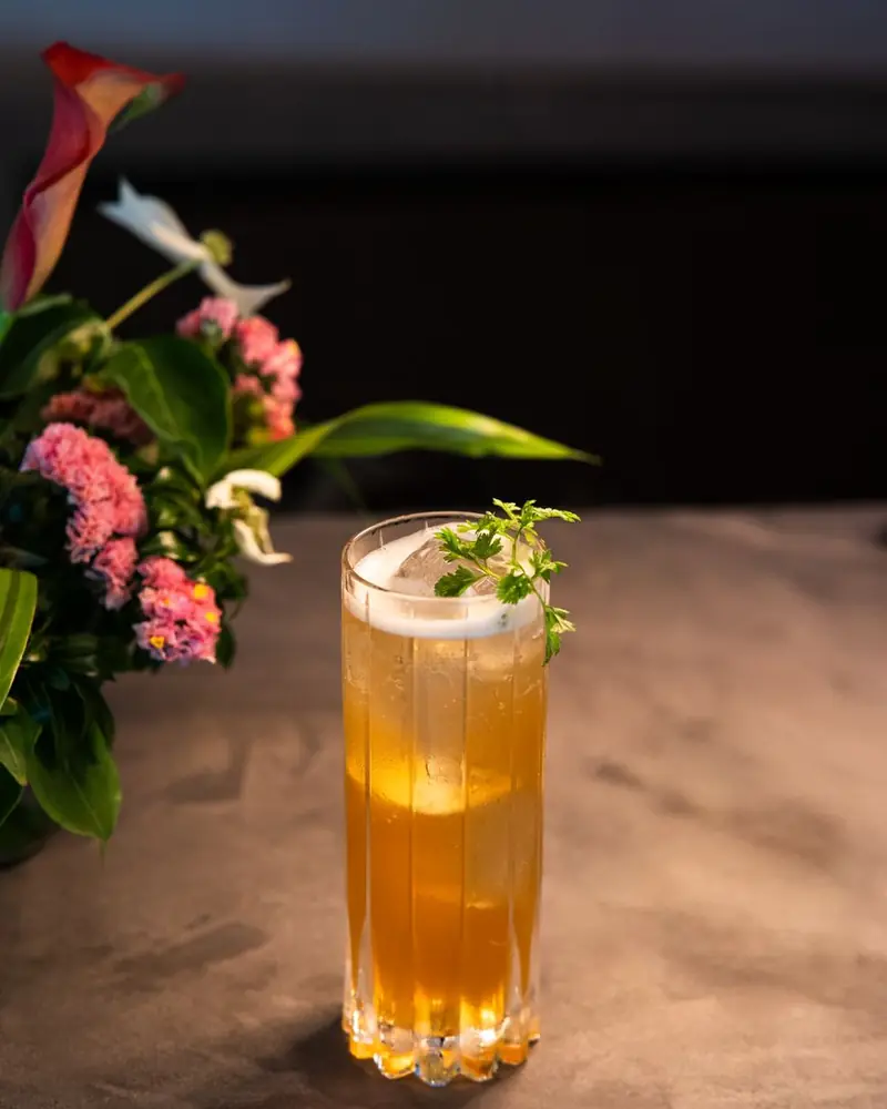 Hohes Glas mit gelber Limonade und Kräutern