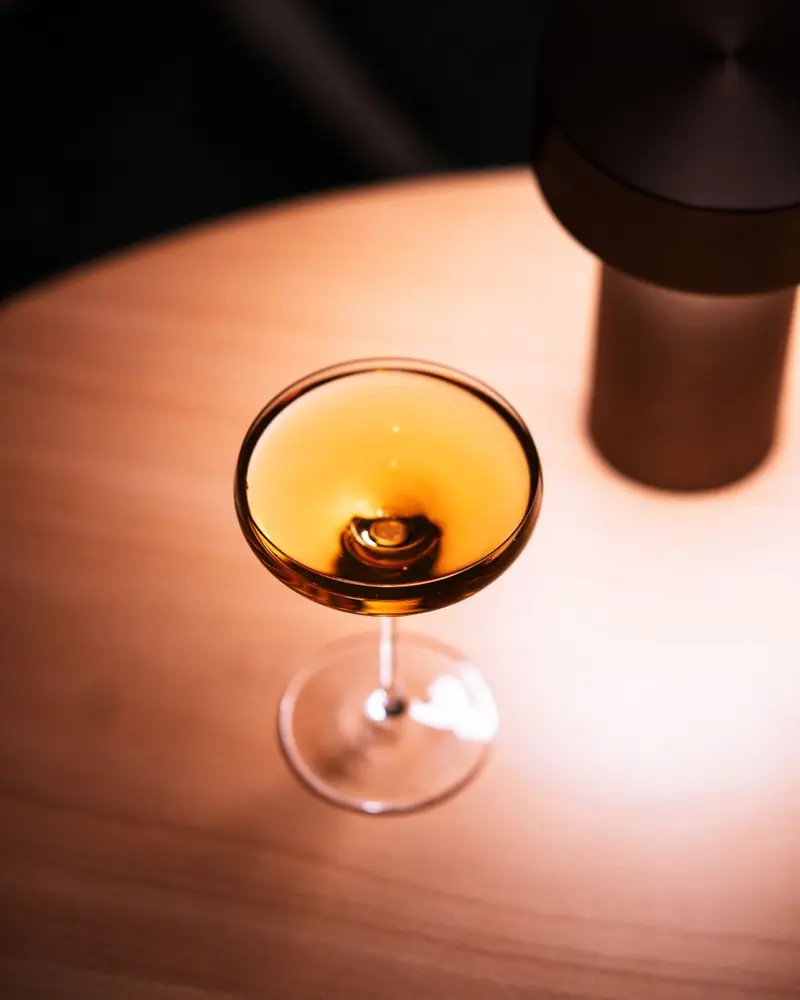 Bernsteinfarbener Drink in einer flachen Schale neben einer Tischleuchte