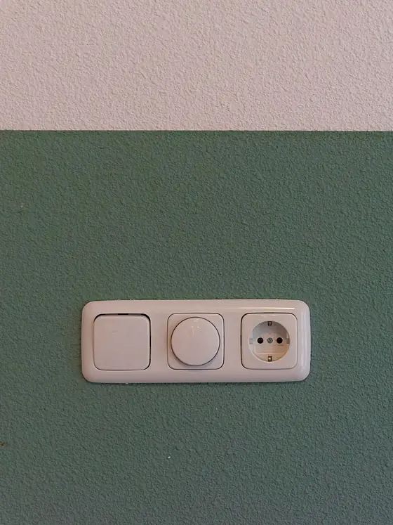 Lichtschalter, Drehdimmer und Steckdose in einem gemeinsamen Rahmen auf einer frisch grün gestrichenen Wand.