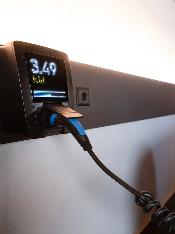 Wallbox an einer Garagenwand, die Anzeige zeigt 3,49 kW Ladeleistung, das Spiralkabel ist eingesteckt, daneben eine Steckdose.