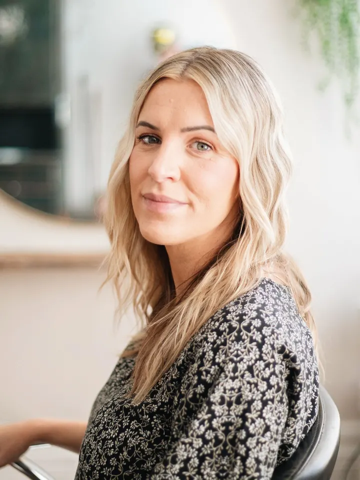 Juli Brandstetter, Inhaberin, mit langem, blondem Haar am Arbeitsplatz vor dem runden Spiegel.