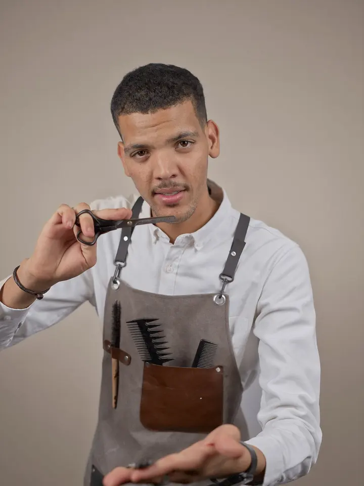 Samir Ajdini in Hemd und Lederschürze, Schere und Kamm in der Hand.