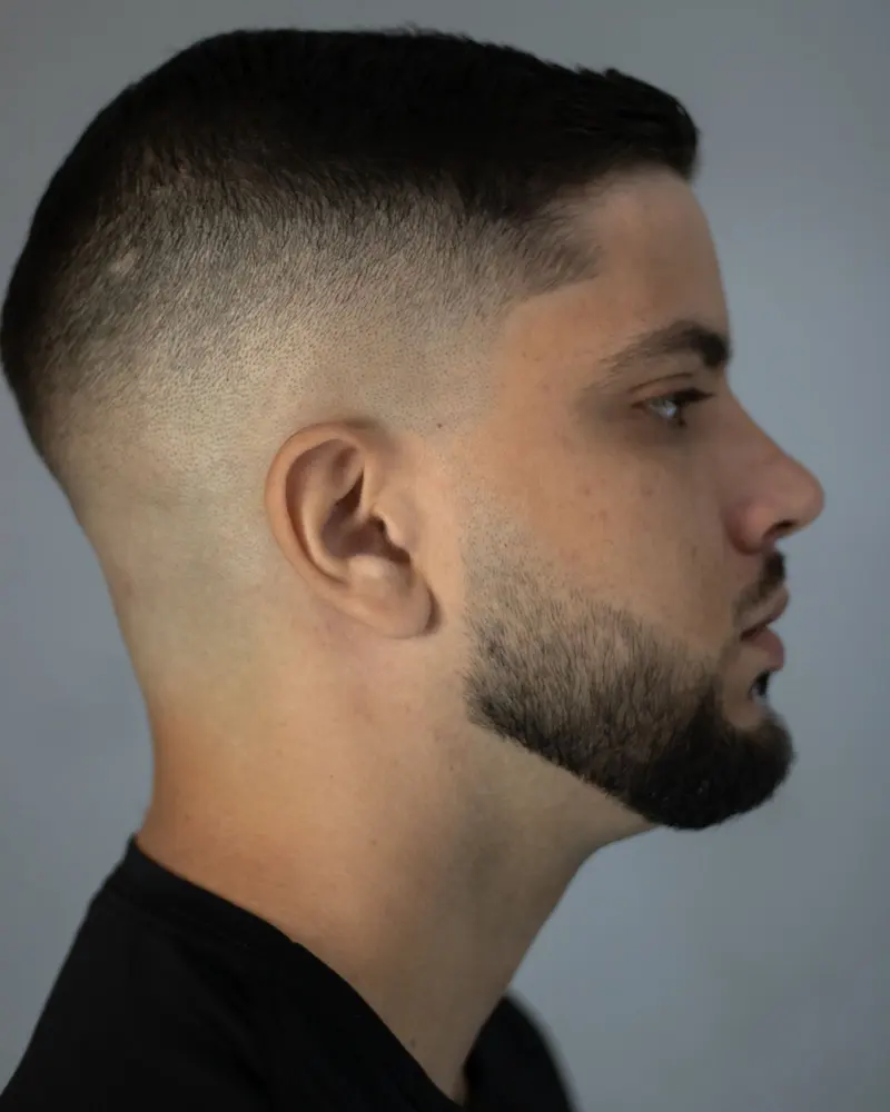 Mann im Profil mit kurzem Fade und sauber konturiertem Bart.
