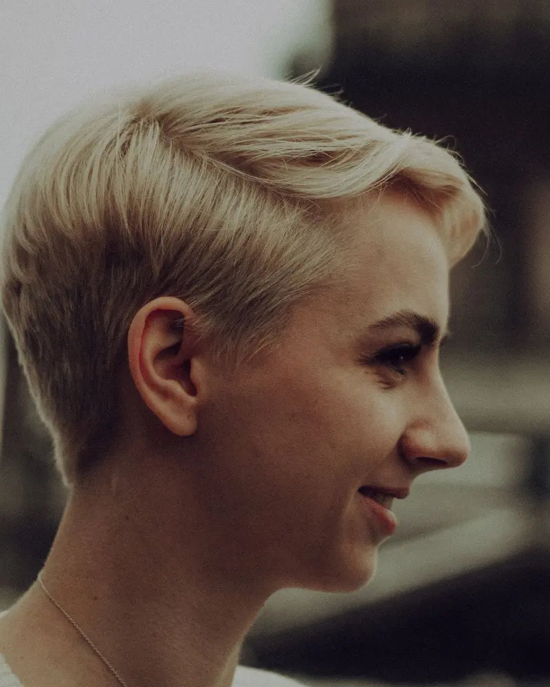 Frau mit hellblondem Pixie-Schnitt im Profil, lächelnd.