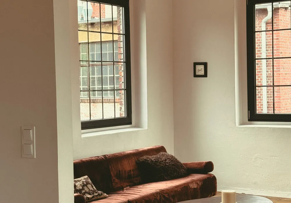Wohnzimmerecke mit Sofa und zwei Fenstern in dickem Mauerwerk.