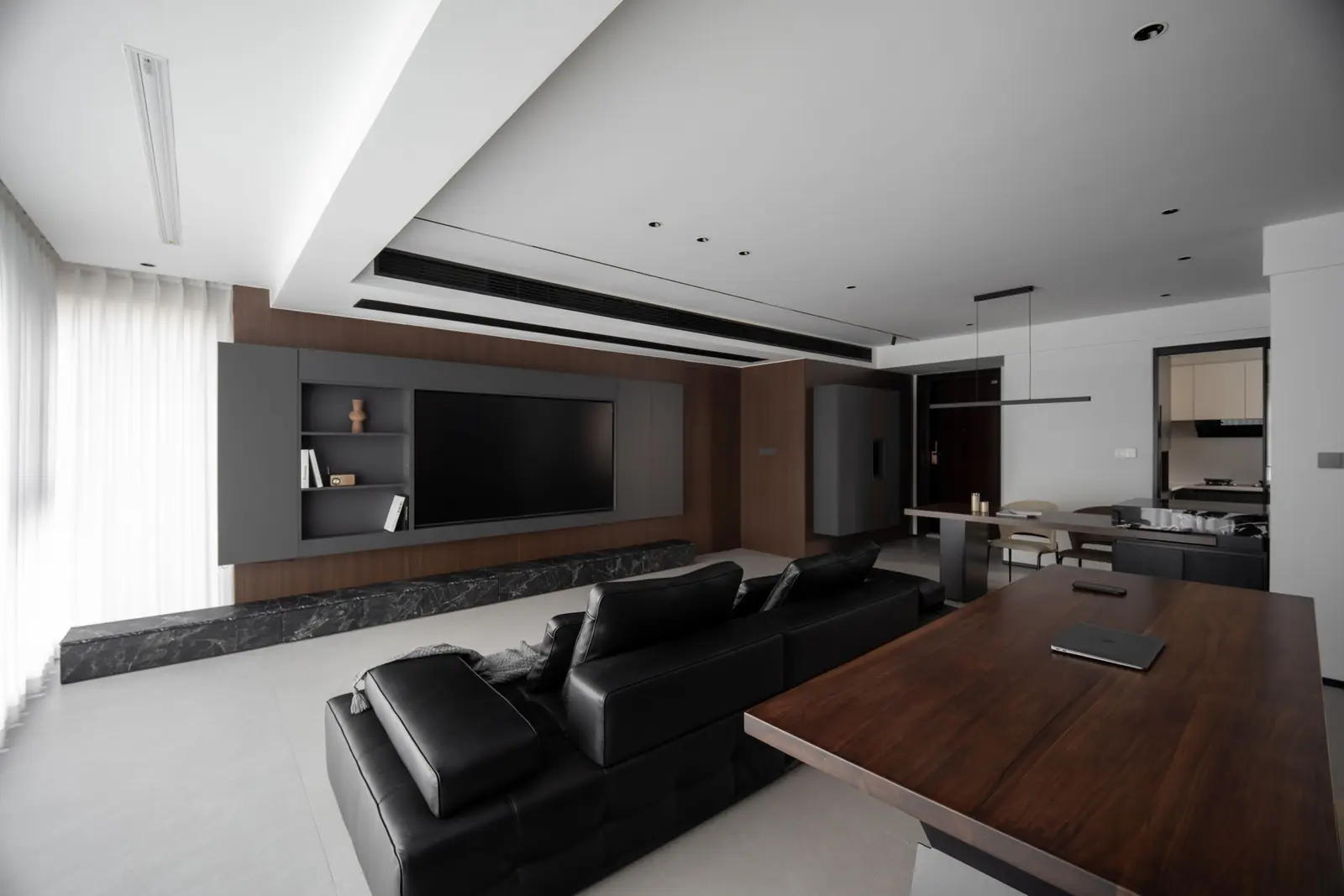 Wohnraum der Wohnung Wieden: Lichtlinien in der Decke, Wand aus Nussholz mit Marmorbank, schwarzes Ledersofa und Esstisch aus Nussholz