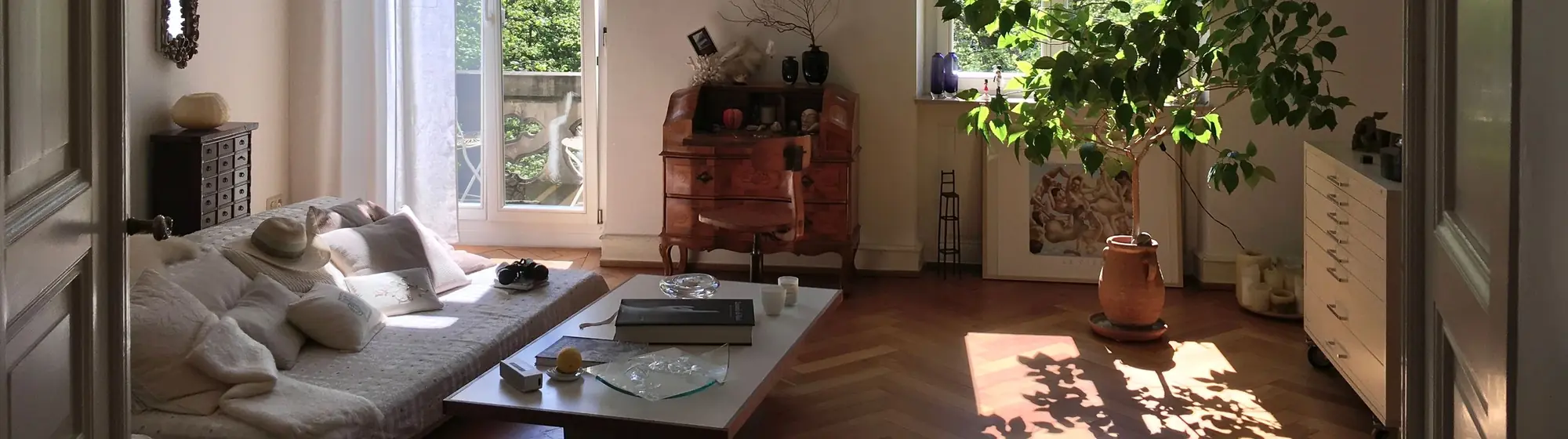 Altbauzimmer mit Fischgrätparkett, Sofa und Pflanzen in der Abendsonne