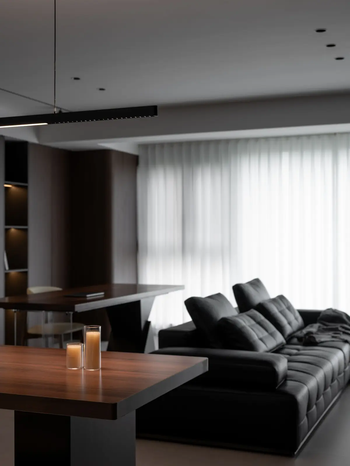 Wohnraum: Ledersofa vor einer Wand aus Nussholz mit offenen Fächern, rechts die Fensterfront mit Vorhängen
