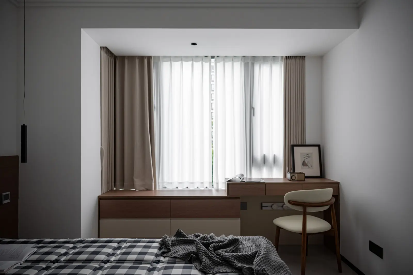 Schlafzimmer mit kariertem Bettüberwurf, Schreibtisch und Stuhl am Fenster